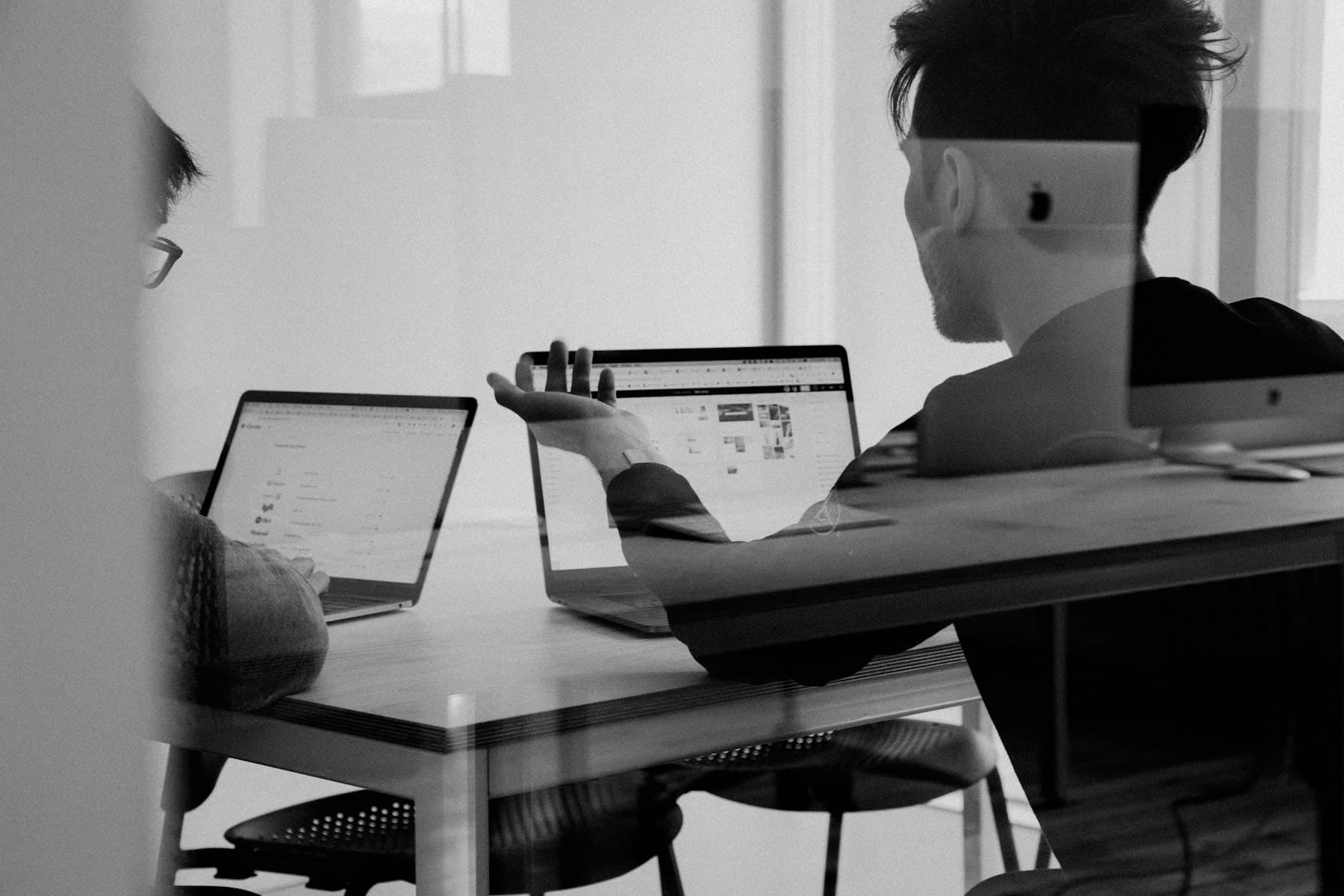 Two people working through a problem together at a desk in a daylit studio.